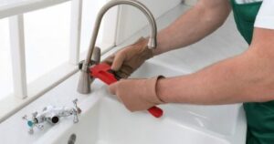 man fixing a water faucet with a red wrench